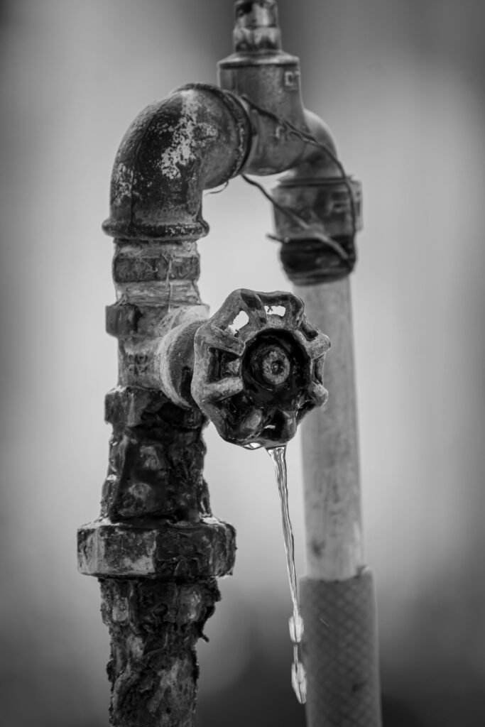 Black and white image of a rusty outdoor faucet dripping water, highlighting decay and nostalgia.